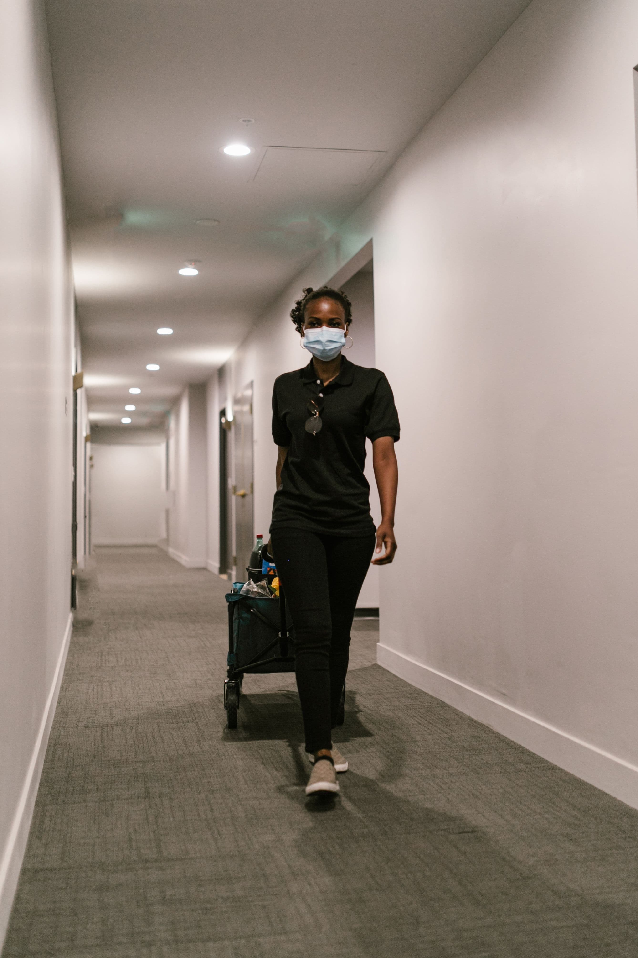 A uniformed janitor walking a corridor with a cleaning cart